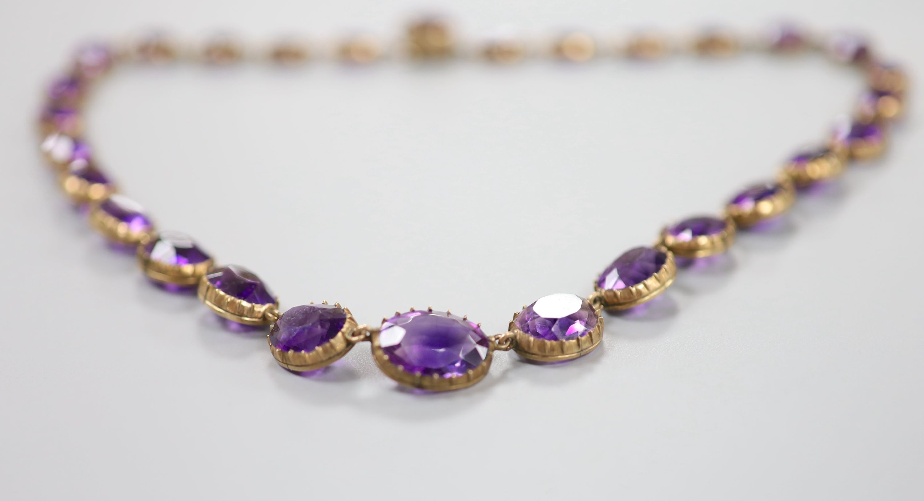 A late Victorian yellow metal and graduated oval cut amethyst set riviere necklace, 39cm, gross weight 37 grams.